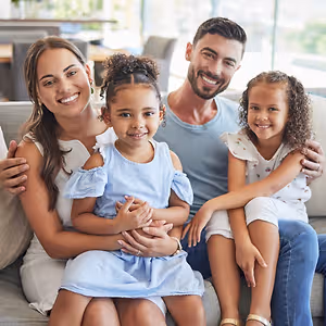 A smiling family of four sitting on a couch, with two girls and their parents.