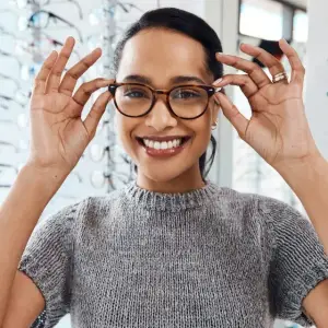 A smiling woman is adjusting her glasses in front of her eyes.