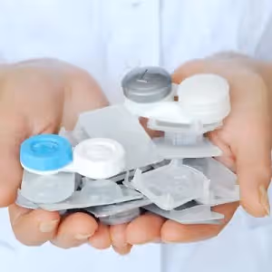 A person in a white shirt holds multiple transparent plastic containers for lenses, likely in a medical setting.