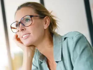 A woman in glasses and a green shirt with her hand on her chin and smiling