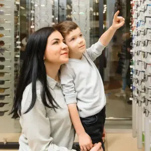 A woman and a boy are standing in front of a glass display case with glasses, and the boy is pointing at one of the glasses.