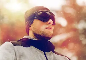 A man with a beard and glasses looks up while wearing a hat and jacket
