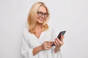 A woman in glasses holding a phone and smiling