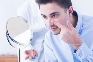 A man touching his eye with his finger and looking at his reflection in a mirror