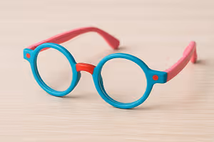 A pair of pink and blue colored glasses with red dots on the sides on a wooden surface