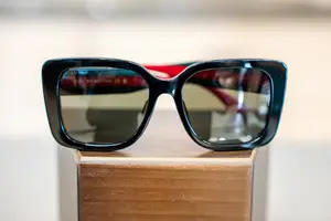A pair of sunglasses with black frames and red accents on a wooden surface.