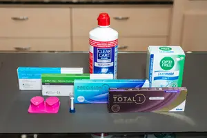 Various eye care products are displayed on a countertop, including boxes of contact lenses and a bottle of contact lens solution.