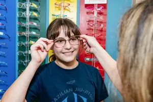 A girl is trying on glasses in a store with a woman helping her.