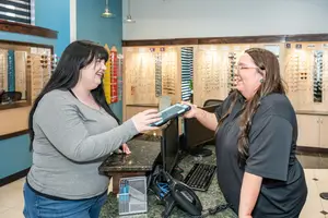 Two women are smiling and laughing while interacting with a tablet at a desk in an office setting