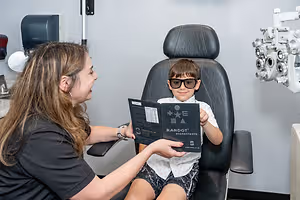 A woman with a young boy in a black leather chair at an optometrist's office.