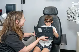 A woman with a young boy in a black leather chair at an optometrist's office.