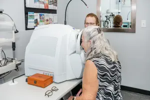 An elderly woman with gray hair is having her eyes examined by a man in an eye clinic.