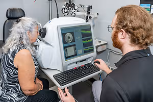 An elderly woman is having her eyes examined by a man in an optometrist's office using a retinal camera