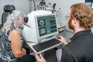 An elderly woman is having her eyes examined by a man in an optometrist's office using a retinal camera