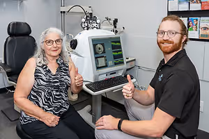 A woman is sitting next to a man in front of an eye examination machine
