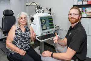 A woman is sitting next to a man in front of an eye examination machine