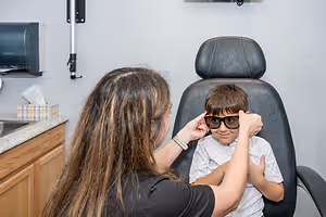 An adult female is adjusting a child's glasses in an optometrist's office.