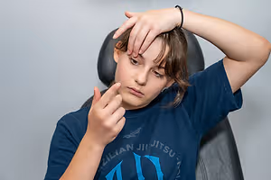 A young person wearing a Brazilian Jiu Jitsu t-shirt and a bracelet removes a contact lens from their eye.