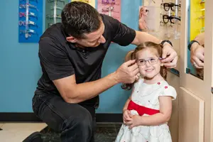 A man adjusting a pair of glasses on a young girl's head.