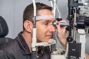 A man is getting an eye exam from an optometrist using a slit lamp to inspect his eye.