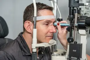 A man is getting an eye exam from an optometrist using a slit lamp to inspect his eye.
