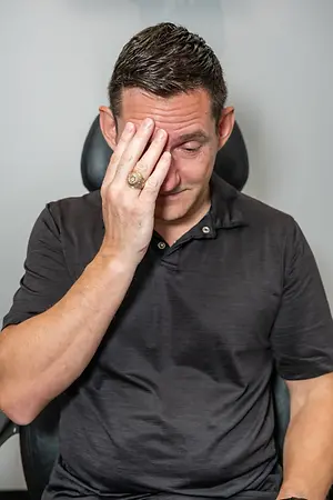 Man sitting in a chair covering his face with his hand