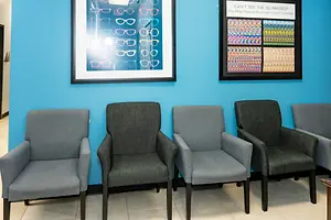 Waiting room with five chairs and framed eyeglass displays on a bright blue wall