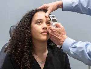 An eye doctor is examining a woman's eye with an ophthalmoscope in a medical clinic.