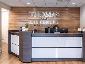The front desk of Thomas Eye Center Optometry with a person working at the desk and a wooden wall behind it.