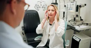 A woman is sitting in a chair and having her eyes examined by a man in a white coat.
