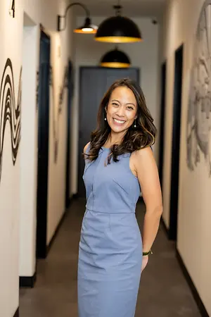 Smiling woman in a blue dress standing in an optometry office hallway