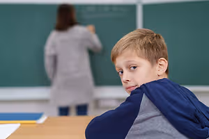 A boy looks at a woman writing on a chalkboard in a classroom