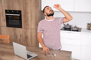 A man holding a thermometer in a kitchen while looking surprised