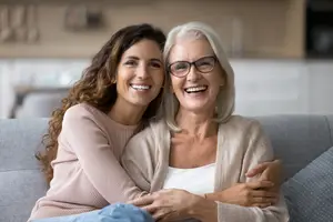 Two women sitting on a couch and smiling at the camera.