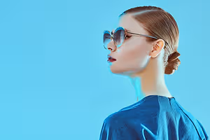 A woman with short brown hair and wearing glasses and a blue top is standing and looking to the left