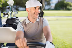 A man drives a golf cart and smiles for the camera at a golf course.