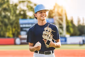 A young baseball player holds a ball and a glove on a baseball field.