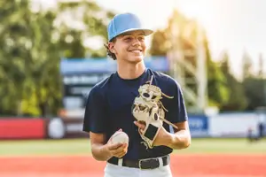 A young baseball player holds a ball and a glove on a baseball field.