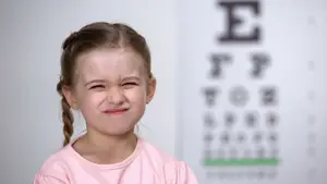 Image of a girl winking and smiling in front of an eye chart.