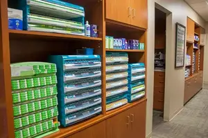 A pharmacy's organized shelves filled with neatly arranged boxes of medications, including some with blue covers and others with green ones, creating a clean and professional atmosphere.