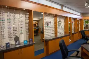 Inside of a eyeglasses store with various frames on display, chairs, and a desk with Converse logo and blue Converse sticker.