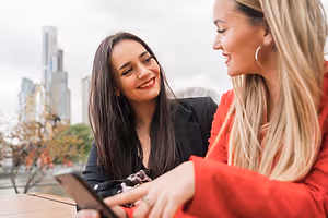 Two women smiling and talking while looking at a cell phone on a table