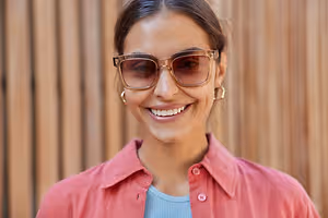 Woman wearing sunglasses smiling in front of a wooden wall