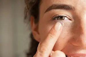 Close-up of a woman placing a contact lens on her eye.