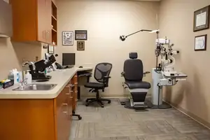 An empty medical examination room with chairs, a sink, and medical equipment