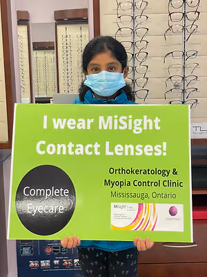 A girl is holding a green sign that says I wear MiSight Contact Lenses in an optical shop.