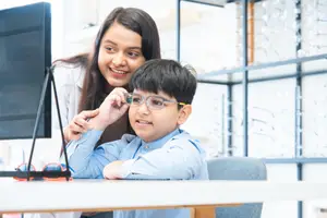 A woman in a lab coat is examining a young boy's glasses on a monitor in a lab