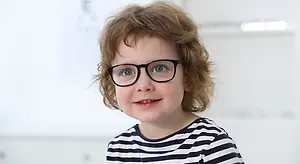 Close up of a young boy wearing glasses and smiling at the camera