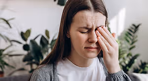 A woman with her eyes closed holding her forehead while looking at the camera
