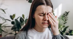 A woman with her eyes closed holding her forehead while looking at the camera